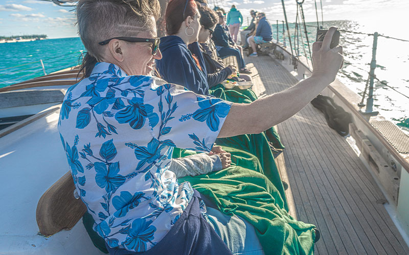 CHL_Affiliates-Main a group of people sitting on a bench on a sailboat, all taking a selfie together