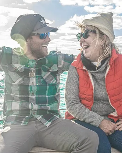 a man and a woman sitting together on a sailboat, smiling and laughing with each other, while out over the water. privacy policy