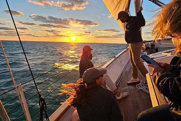 CHL_Contact-KeyWest a group of classic harbor line crew members chatting on a sailboat, looking out towards a sunset in the distance