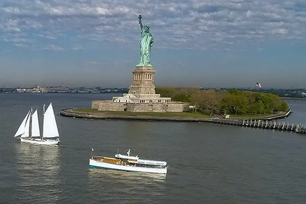 CHL_Contact-NYC a helicopter view of the statue of liberty with a sailboat and a motor yacht from classic harbor line seen on the water