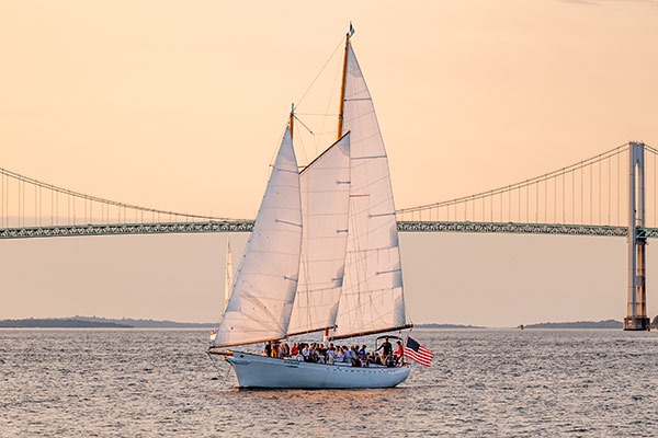 CHL_Contact-Newport a classic harbor line sailboat cruising across the water with a giant arch bridge behind it