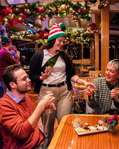 Crew member serving drinks to customers on the yacht Manhattan with the grand salon decked out in holiday decor